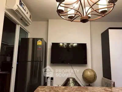 Modern living room with stylish chandelier, wall-mounted TV, and sleek refrigerator.