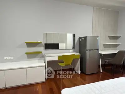 Modern bedroom with sleek furniture and stainless steel fridge on wooden flooring.