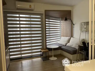 Modern cozy living room with natural light filtering through wooden blinds, featuring a comfortable L-shaped sofa, sleek furniture, and warm wooden flooring.