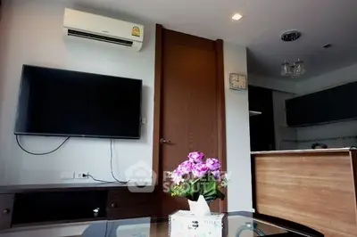 Modern living room with wall-mounted TV and air conditioning, featuring stylish decor and open kitchen layout.