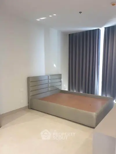 Spacious bedroom with modern bed frame and large windows with curtains.