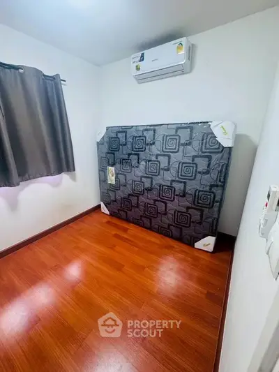 Cozy bedroom with wooden flooring and air conditioning, featuring a neatly wrapped mattress against the wall.