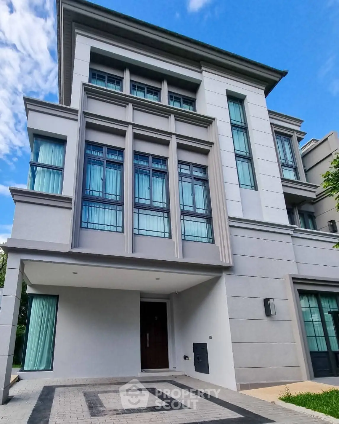 Modern multi-story residential building with large windows and driveway.