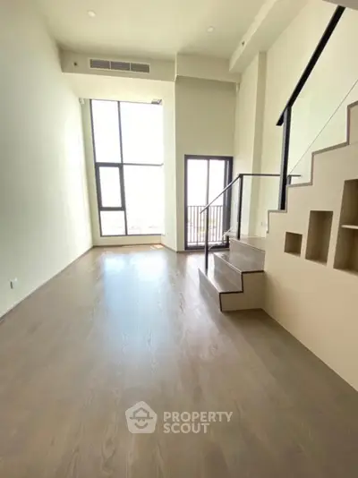 Spacious modern loft with high ceilings and large windows offering natural light and a small balcony.