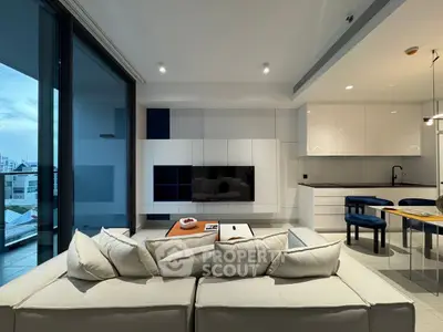 Modern living room with open kitchen and large balcony view, featuring sleek white cabinetry and cozy seating.