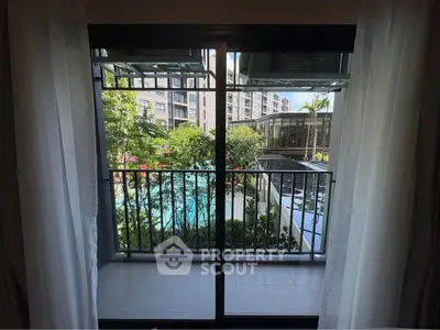 Charming balcony view overlooking lush garden and pool in modern apartment complex.