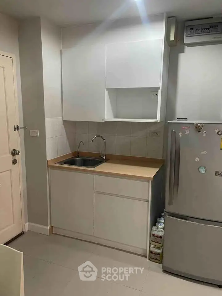 Compact kitchen with modern cabinetry and stainless steel fridge in cozy apartment.