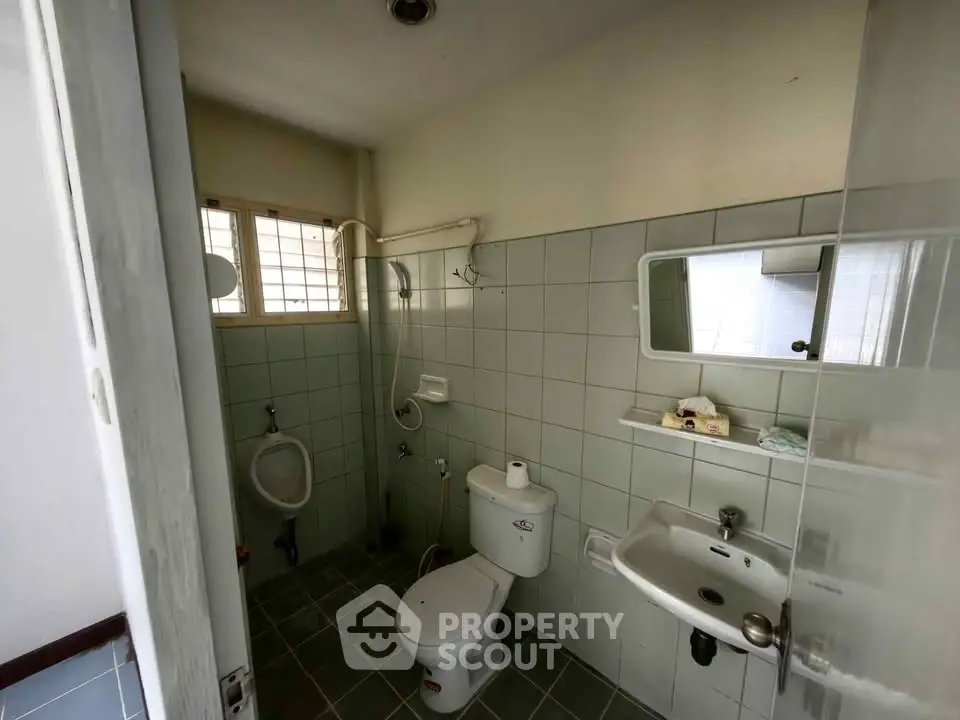 Compact bathroom with shower, toilet, and sink in a tiled setting.