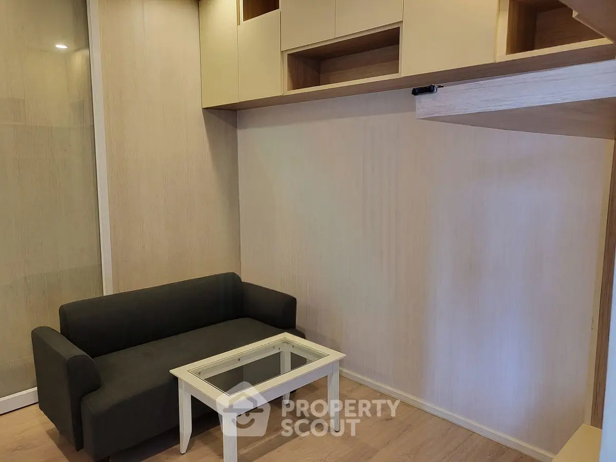 Modern living room with sleek black sofa and glass-top coffee table, featuring built-in wooden storage units.