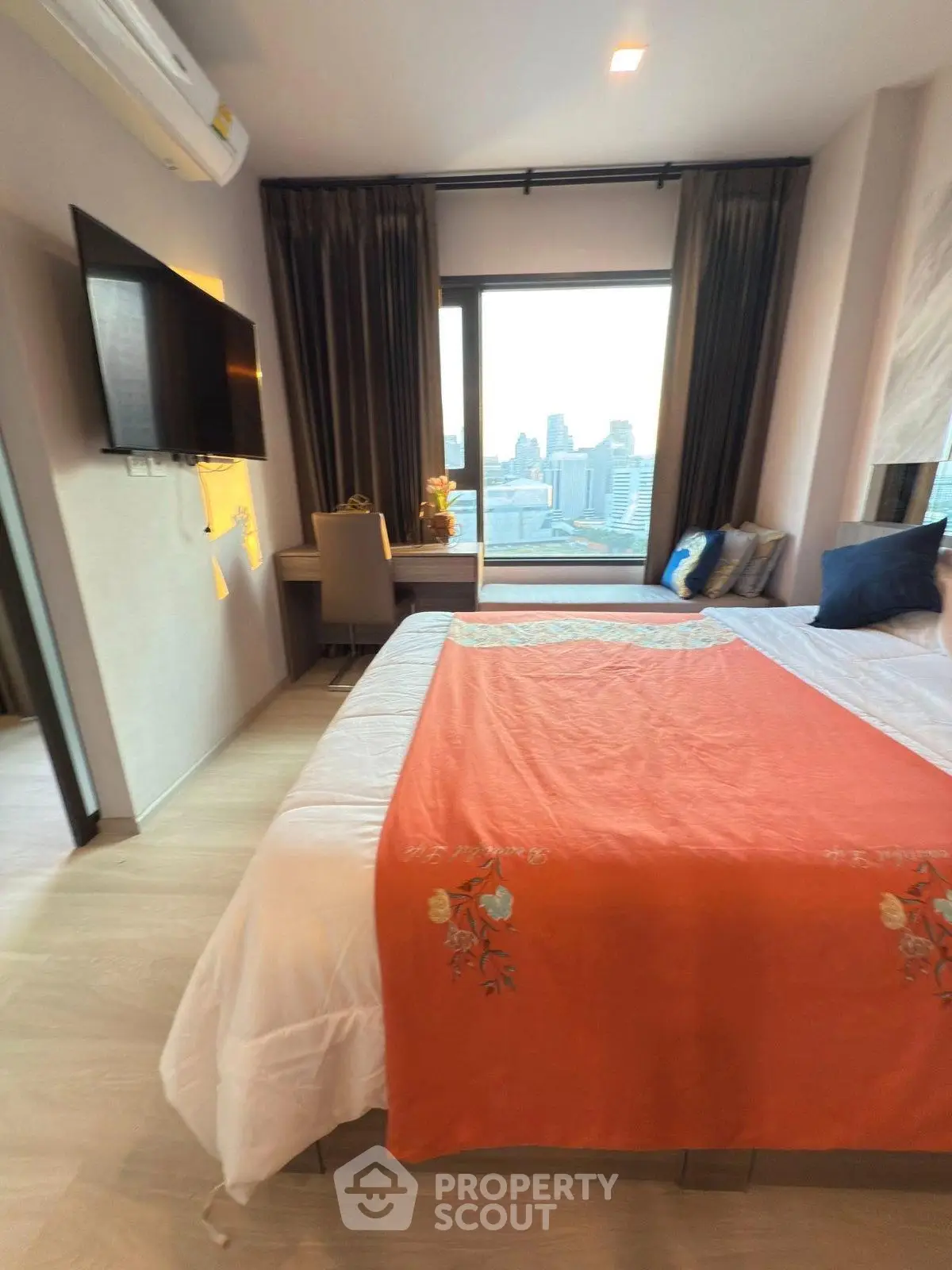 Modern bedroom with city view, featuring a large window, stylish decor, and a wall-mounted TV.