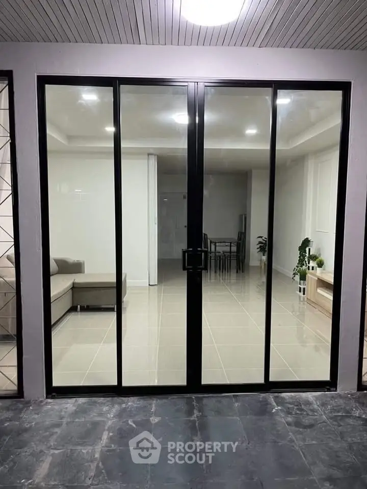 Modern interior view through glass doors showcasing a stylish living room with sleek furniture.