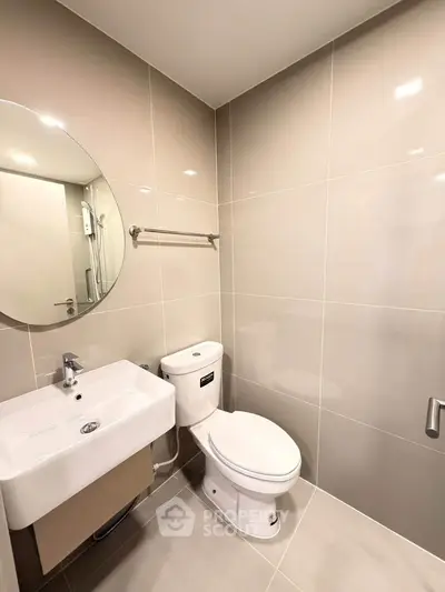 Modern bathroom with sleek fixtures and neutral tiles, featuring a round mirror and compact sink.