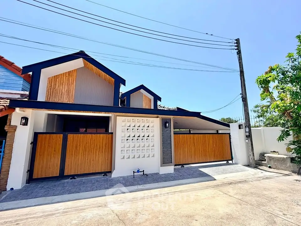 Modern two-story house with wooden accents and gated driveway under clear blue sky.