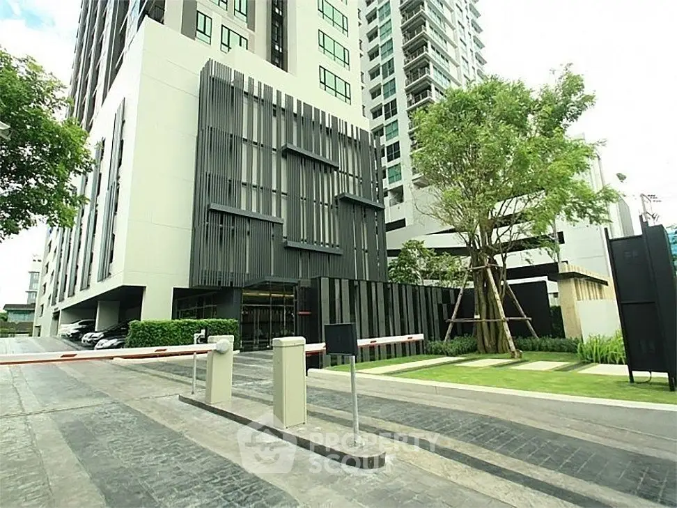 Modern high-rise building entrance with sleek design and lush landscaping.