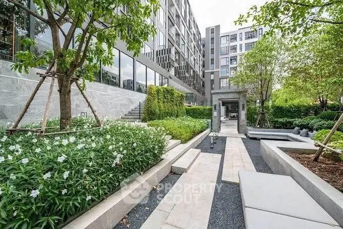 Modern apartment building with lush landscaped garden and seating area.