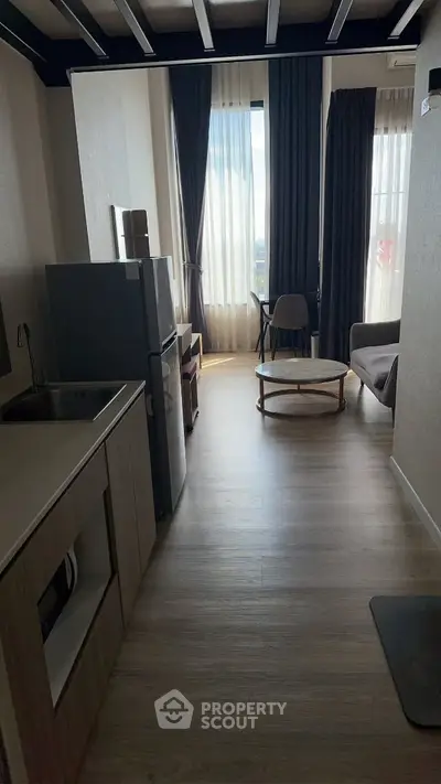Modern apartment interior with open kitchen and cozy living area, featuring large windows and stylish decor.