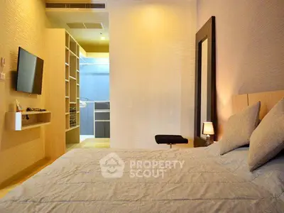 Modern bedroom with cozy bedding and wall-mounted TV, featuring a walk-in closet.