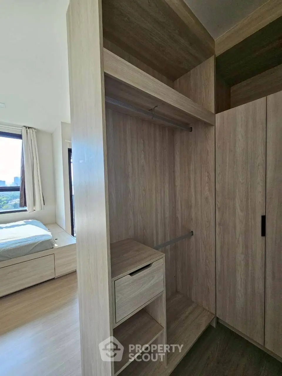 Spacious bedroom with modern wooden walk-in closet and large window view.