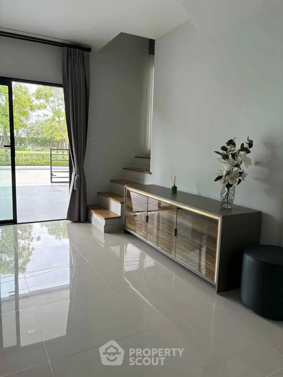 Modern living room with sleek staircase and glass doors opening to a lush garden view.