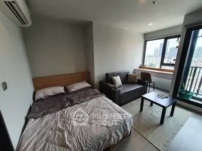 Modern studio apartment with bed, sofa, and city view from window.