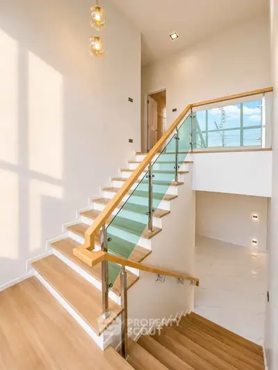 Elegant modern staircase with glass railing and wooden steps in a bright, airy home interior.