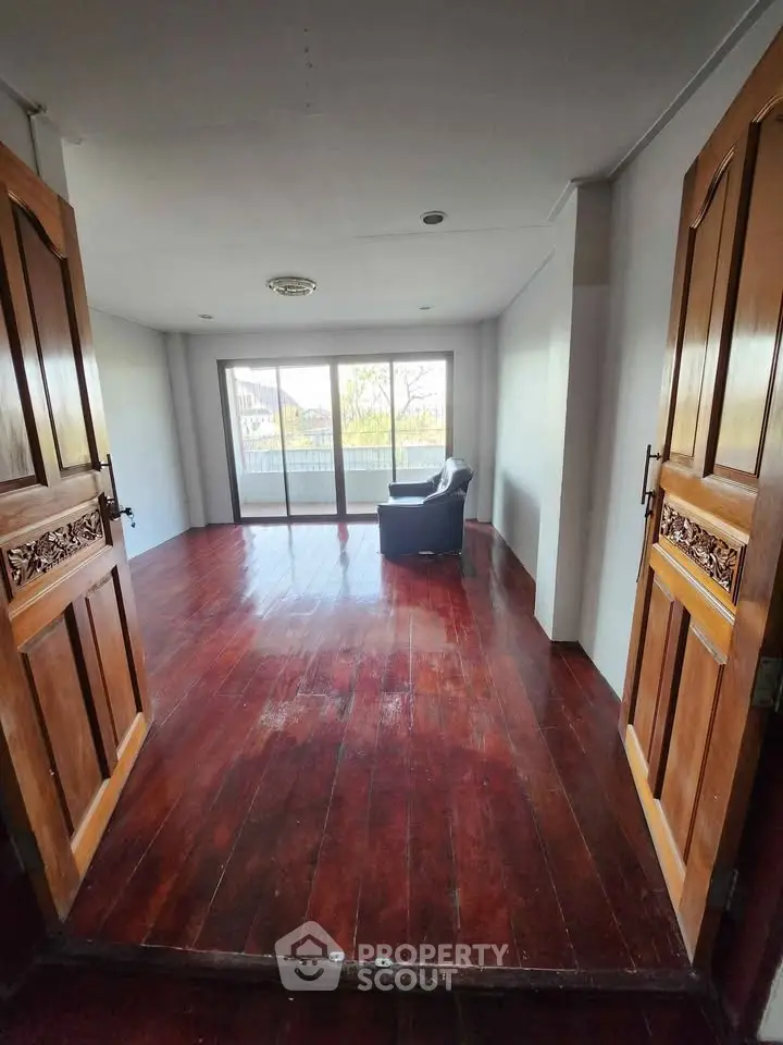Spacious living room with wooden floors and large windows offering natural light and a serene view.