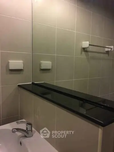 Modern bathroom with sleek black countertop and beige tiles, featuring a stylish faucet and towel rack.