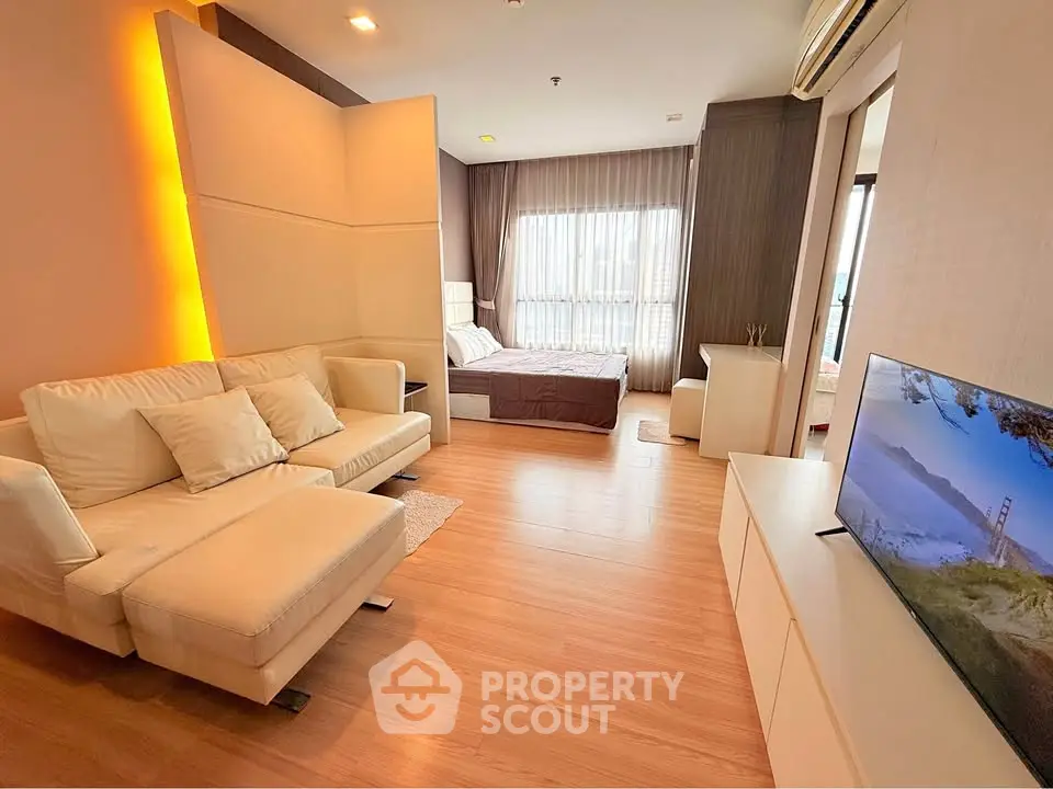 Modern open-plan living room with cozy seating and bedroom area, featuring stylish decor and natural light.