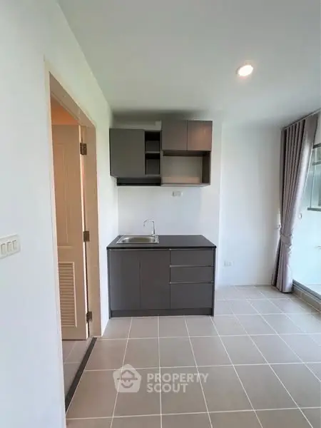 Modern compact kitchen with sleek cabinets and tiled flooring in a bright apartment.