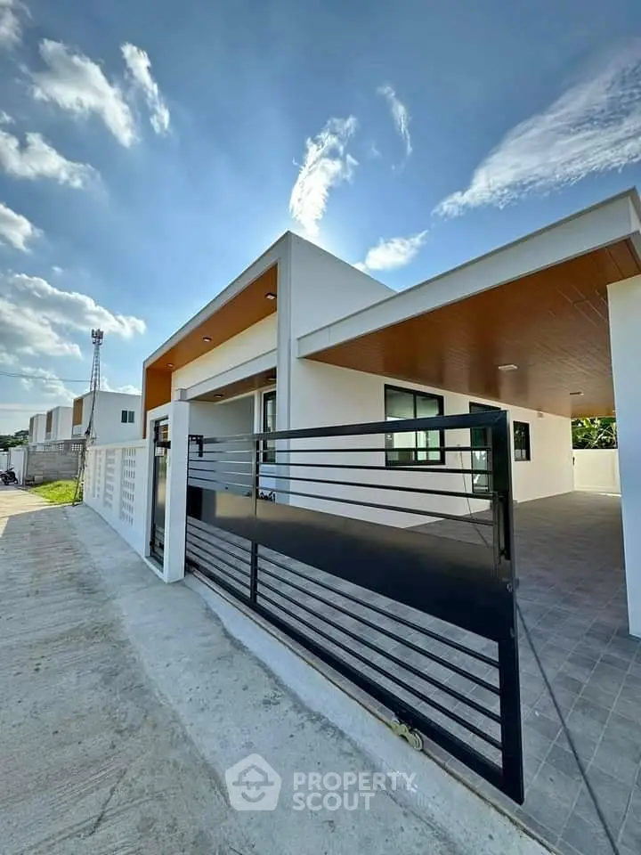 Modern single-story house with sleek black gate and spacious driveway under a clear blue sky.