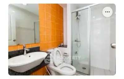 Modern bathroom with orange tiles and glass shower enclosure.