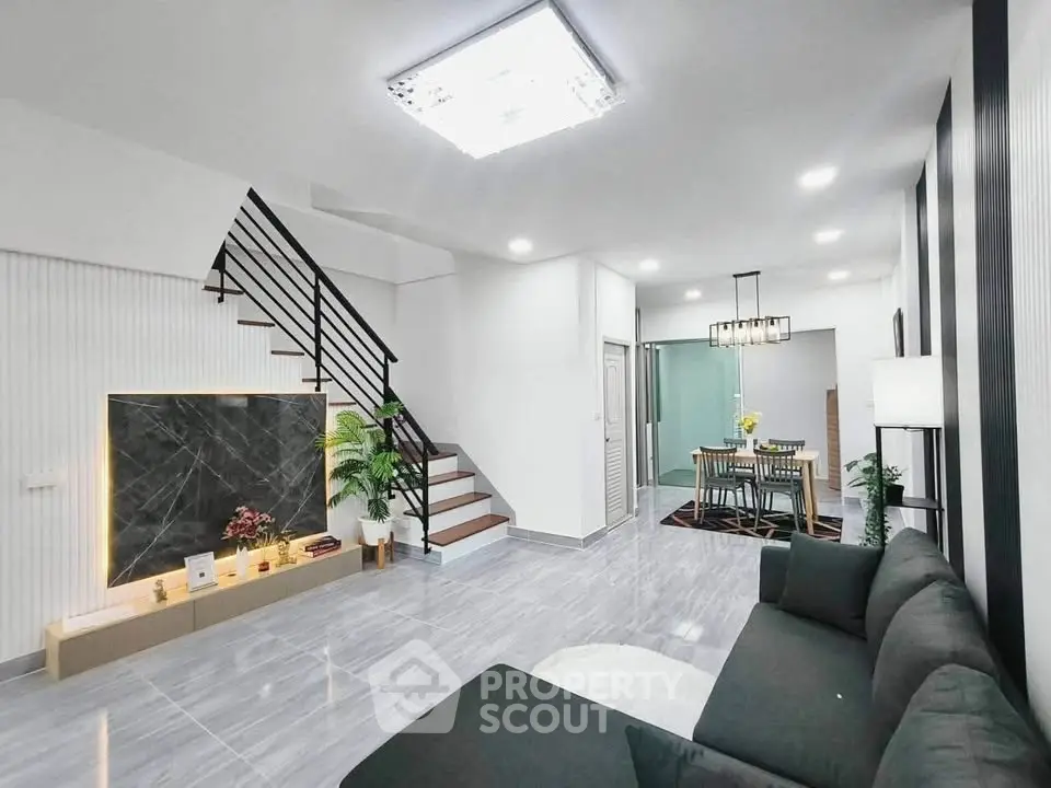 Modern open-plan living room with sleek staircase and dining area, featuring contemporary decor.