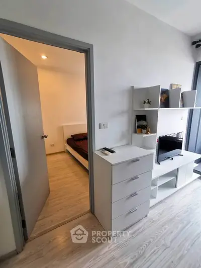 Modern apartment interior with sleek white furniture and open doorway to bedroom, showcasing minimalist design.