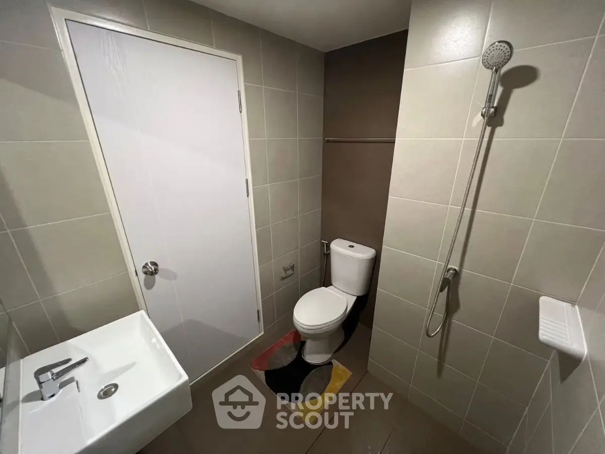 Modern bathroom with sleek fixtures and neutral tiles, featuring a shower and toilet.