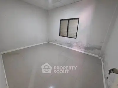 Spacious empty room with tiled flooring and a window, ideal for customization.