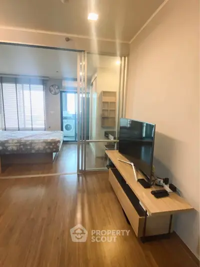 Modern apartment interior with sliding glass doors, TV unit, and bedroom view.