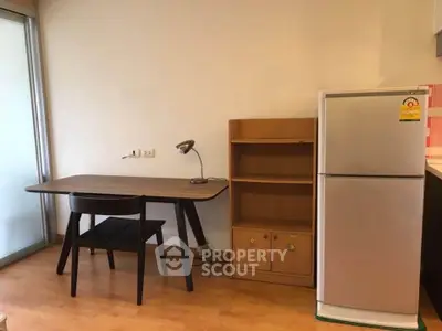 Cozy study area with wooden desk, chair, and fridge in modern apartment.