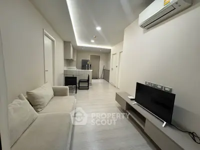 Modern living room with sleek design, featuring a comfortable sofa, flat-screen TV, and open kitchen layout.