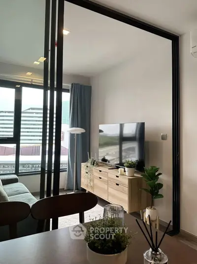 Modern living room with sleek furniture and large TV, featuring a city view through glass doors.