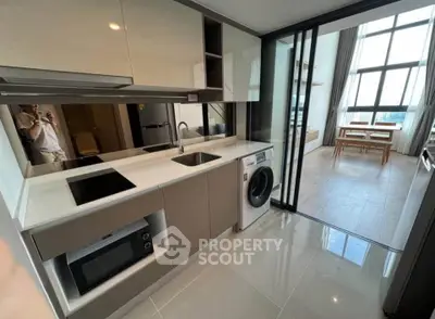 Modern kitchen with sleek appliances and open layout leading to bright dining area with large windows.