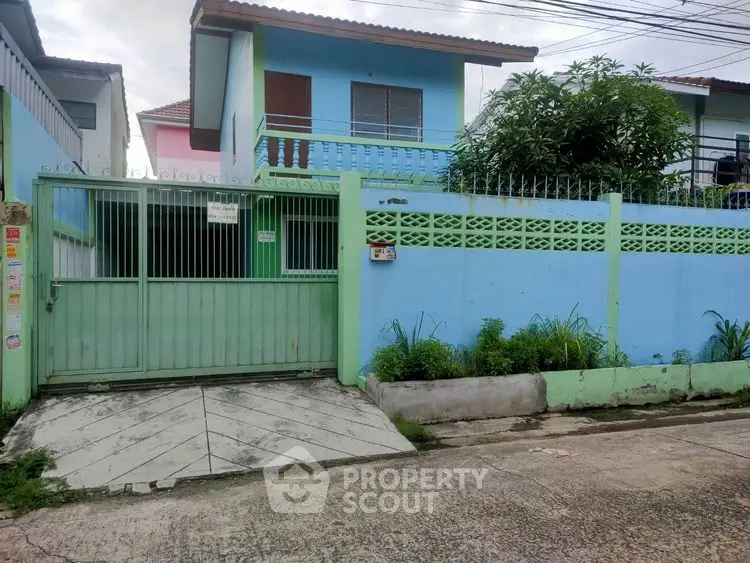 Charming two-story blue house with gated entrance and lush greenery