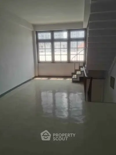 Spacious loft-style living area with large windows and modern staircase, perfect for urban living.