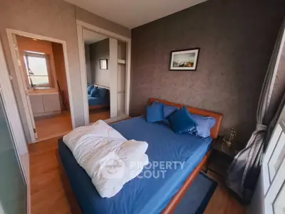 Cozy bedroom with blue bedding and mirrored closet doors, offering a glimpse into the bathroom.