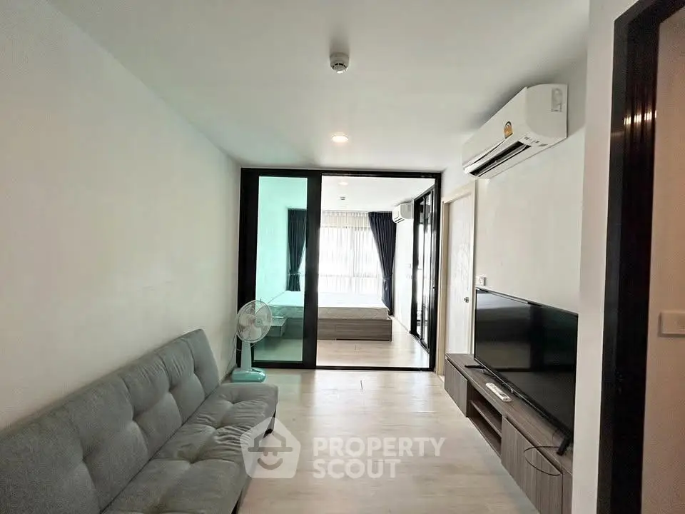 Modern living room with sleek design and air conditioning, leading to a bright bedroom through glass doors.