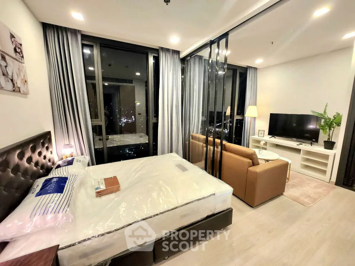 Modern studio apartment with open layout, featuring a cozy living area and large windows offering city views.