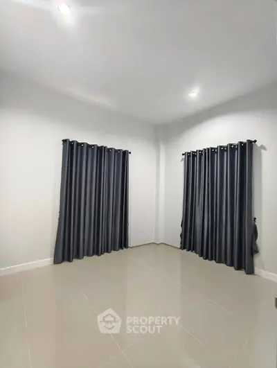 Spacious empty room with tiled floor and dark curtains, ideal for customization.