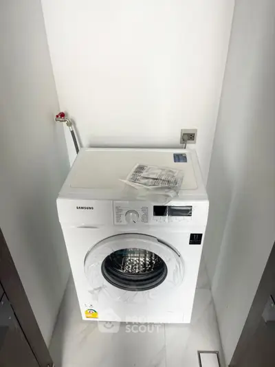 Modern Samsung washing machine in a sleek laundry nook with white walls and marble flooring.
