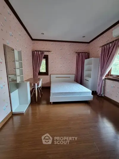 Charming bedroom with pink floral wallpaper and natural light, featuring a cozy bed and stylish furniture.