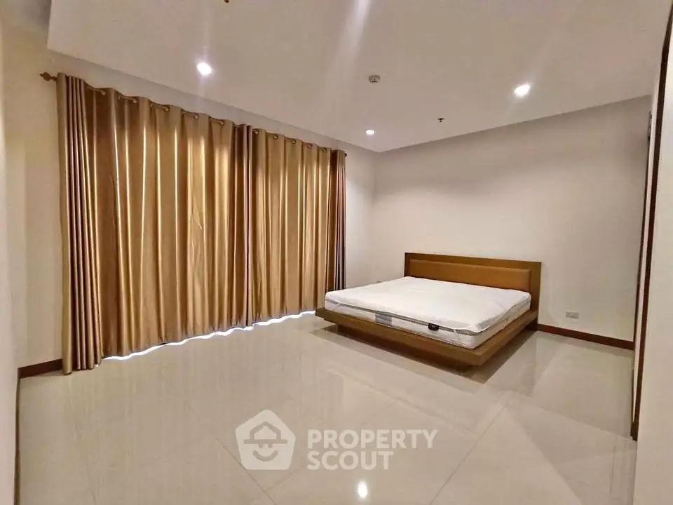 Spacious bedroom with large windows and elegant curtains in modern apartment.