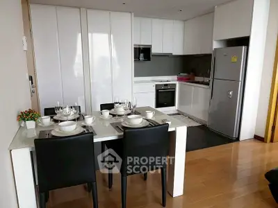 Modern kitchen with sleek white cabinets and dining area, featuring stainless steel appliances.